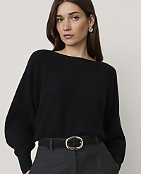 A woman in a black sweater and grey pants stands against a plain background. carousel Product Image 1