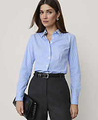 A woman in a blue pinstripe shirt and dark pants holds a black clutch in front of a plain background. carousel Product Image 1