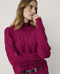 A woman in a magenta cable-knit sweater and pink pants poses against a plain white background. carousel Product Image 1