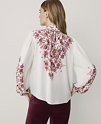 A woman in a white blouse with a floral pattern stands against a plain background. carousel Product Image 2