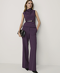 A woman in a purple pantsuit with a cowl neck and a black clutch stands against a plain white background. carousel Product Image 3
