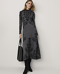 A woman in a grey patterned dress and black boots stands with a black tote bag against a plain white background. carousel Product Image 1