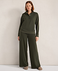 A woman stands in a dark green loungewear set with wide-leg pants and a collared top, against a plain, textured wall. carousel Product Image 1
