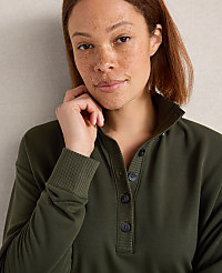 A woman with freckles and short brown hair, wearing a green collared sweatshirt, is looking towards the camera with her hand near her face, against a plain, light-colored background. carousel Product Image 2
