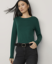 A woman in a green long-sleeved shirt and black jeans with a black belt stands against a plain white background. carousel Product Image 1