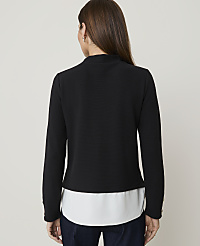 A woman in a black textured jacket over a white blouse stands against a plain, light-colored background. carousel Product Image 2