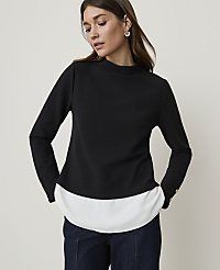 A woman in a black mock-neck top layered over a white shirt stands against a plain, light background. carousel Product Image 1