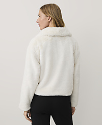 A woman wearing a white faux-fur jacket and black trousers stands against a plain, light-colored background. carousel Product Image 2