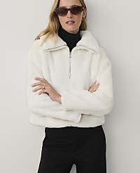A woman wearing a white faux-fur jacket, black turtleneck, and sunglasses stands with crossed arms against a plain white background. carousel Product Image 1