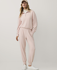 A woman wearing a light pink tracksuit, a tan cap, and white sneakers stands against a plain white background. carousel Product Image 1