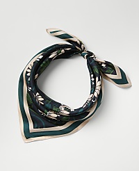 A floral-patterned green and cream silk scarf is tied in a knot against a plain light gray background. carousel Product Image 1