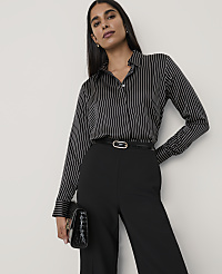 A woman wearing a black and white striped shirt and black trousers stands against a plain white background. carousel Product Image 1