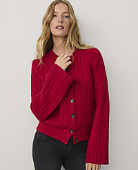 A woman wearing a red cable-knit cardigan and black jeans stands against a plain, light-colored background. carousel Product Image 1