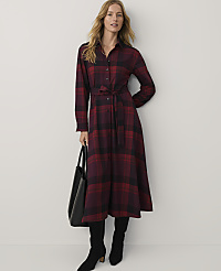 A woman wearing a red and black plaid maxi dress and black boots stands against a plain white background while holding a black handbag. carousel Product Image 1