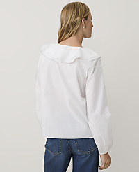 A woman wearing a white ruffled blouse and blue jeans stands with her back to the camera against a plain light gray background. carousel Product Image 2