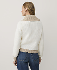 A woman wearing a white ribbed sweater with beige trim and blue jeans stands against a plain white background. carousel Product Image 2