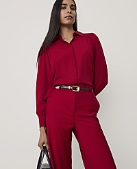 A woman wearing a red button-down shirt and matching trousers with a dark belt stands against a plain, light-colored background. carousel Product Image 1