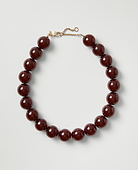 A necklace of polished deep red beads with a gold clasp rests on a plain light gray background. carousel Product Image 1