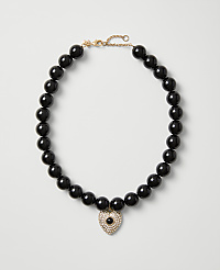 A necklace of polished black beads with a heart-shaped crystal pendant rests on a plain light gray background. carousel Product Image 1