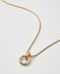 A gold snake chain necklace with a circular pendant rests on a plain white background. carousel Product Image 2
