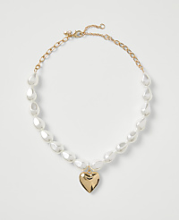 A gold-toned necklace with white teardrop pearls and a heart pendant rests on a plain white background. carousel Product Image 1