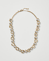 A gold-toned necklace with clear crystal stones is centered against a plain light gray background. carousel Product Image 1