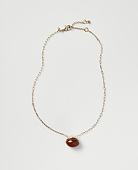 A gold chain necklace with a red oval gemstone pendant rests against a plain light gray background. carousel Product Image 1