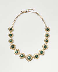 A gold chain necklace featuring green circular gemstones is centered against a plain light gray background. carousel Product Image 1