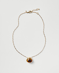 A gold chain necklace with a brown oval pendant rests on a plain light gray background. carousel Product Image 1