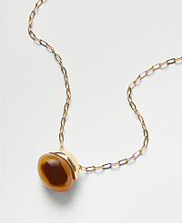 A gold chain necklace with a round, amber-colored stone pendant rests on a plain white background. carousel Product Image 2
