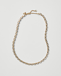 A gold-toned necklace with clear crystals is laid out against a plain, light gray background. carousel Product Image 1