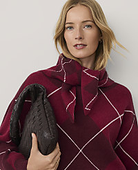 A blonde woman wearing a burgundy plaid sweater and holding a dark brown woven handbag poses against a plain light gray background. carousel Product Image 1