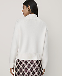 A woman wearing a white turtleneck sweater and a plaid skirt stands against a plain, light-colored background. carousel Product Image 2
