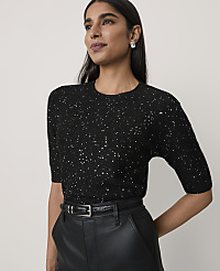 A woman wearing a sparkling black top and leather trousers stands against a plain, light-colored background. carousel Product Image 1