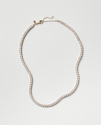A sparkling tennis necklace with clear stones rests on a plain, light gray background. carousel Product Image 1
