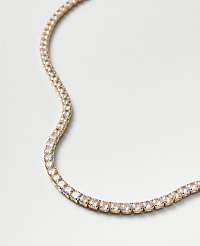 A sparkling tennis necklace with clear stones in a gold setting curves across a plain, light gray background. carousel Product Image 2