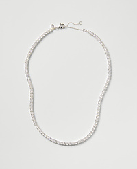 A sparkling tennis necklace with clear stones rests against a plain, light gray background. carousel Product Image 1