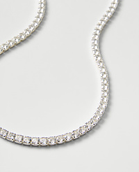 A sparkling tennis necklace of clear gemstones curves across a plain, light gray background. carousel Product Image 2