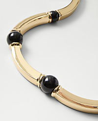 A gold-toned curved necklace with black spherical beads rests on a plain white background. carousel Product Image 2