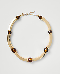A gold-toned necklace with amber-colored beads rests on a plain light gray background. carousel Product Image 1