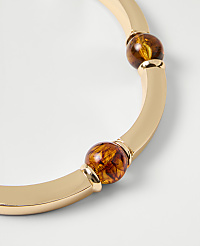 A gold-toned bangle with amber-colored beads rests against a plain white background. carousel Product Image 2