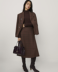 A woman wearing a brown plaid suit and boots holds a dark purple handbag against a plain white background. carousel Product Image 1