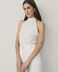 A woman wearing a white pleated halter top and white trousers stands against a plain, light-colored background. carousel Product Image 1