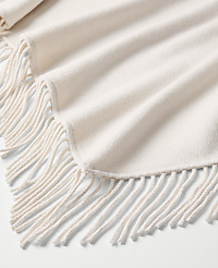 A cream-colored fringed blanket is draped in soft folds over a plain white background. carousel Product Image 2