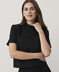 A woman wearing a black short-sleeved top and gold jewelry poses against a plain, light-colored background. carousel Product Image 1