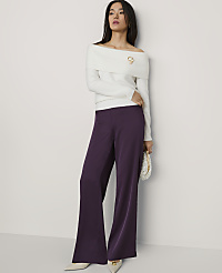 A woman wearing a white off-the-shoulder sweater and wide-leg purple trousers stands against a plain white wall. carousel Product Image 4