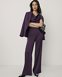 A woman wearing a purple satin suit and holding a black clutch stands against a plain white background. carousel Product Image 1