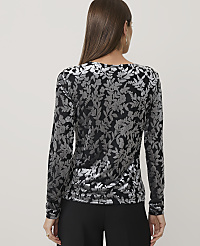 A woman wearing a black and silver floral print top and black trousers stands against a plain light grey background. carousel Product Image 2