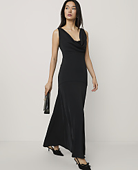 A woman wearing a long black cowl-neck dress and black heels stands against a plain, light-colored background. carousel Product Image 3