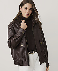 A woman wearing a dark brown leather jacket, a brown turtleneck, and white pants stands against a plain, light-colored background. carousel Product Image 1